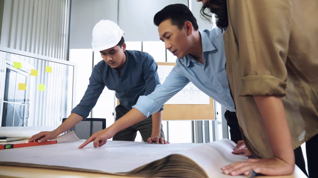 Team of young Asian architects discussing on construction site.